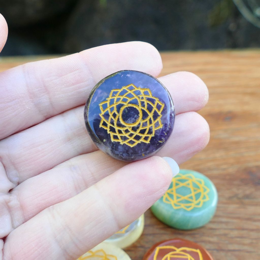 Set of seven polished crystal chakra stones engraved with gold chakra symbols for meditation, Reiki, chakra balancing, and energy healing.