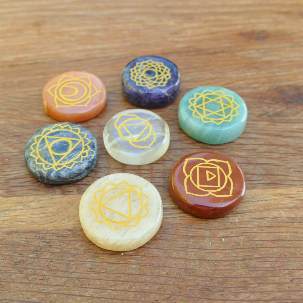 Set of seven polished crystal chakra stones engraved with gold chakra symbols for meditation, Reiki, chakra balancing, and energy healing.