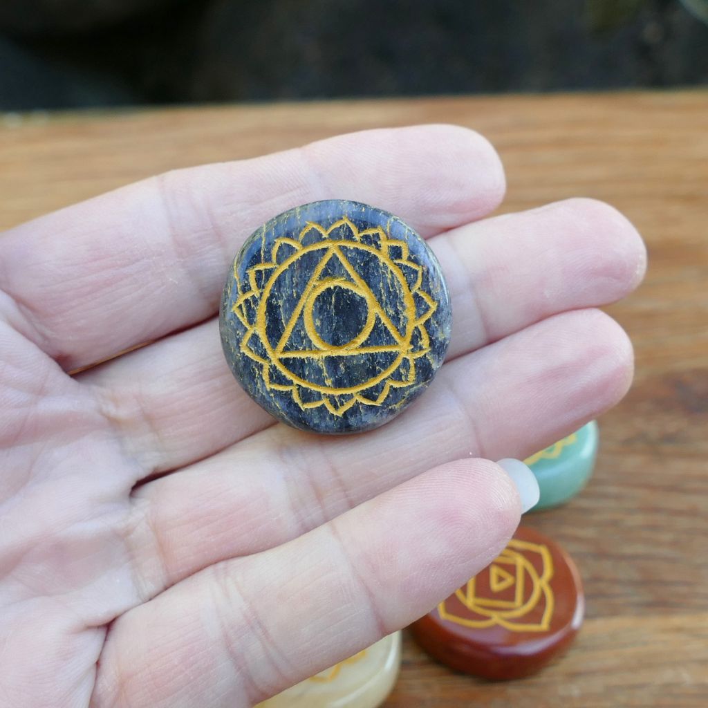 Set of seven polished crystal chakra stones engraved with gold chakra symbols for meditation, Reiki, chakra balancing, and energy healing.